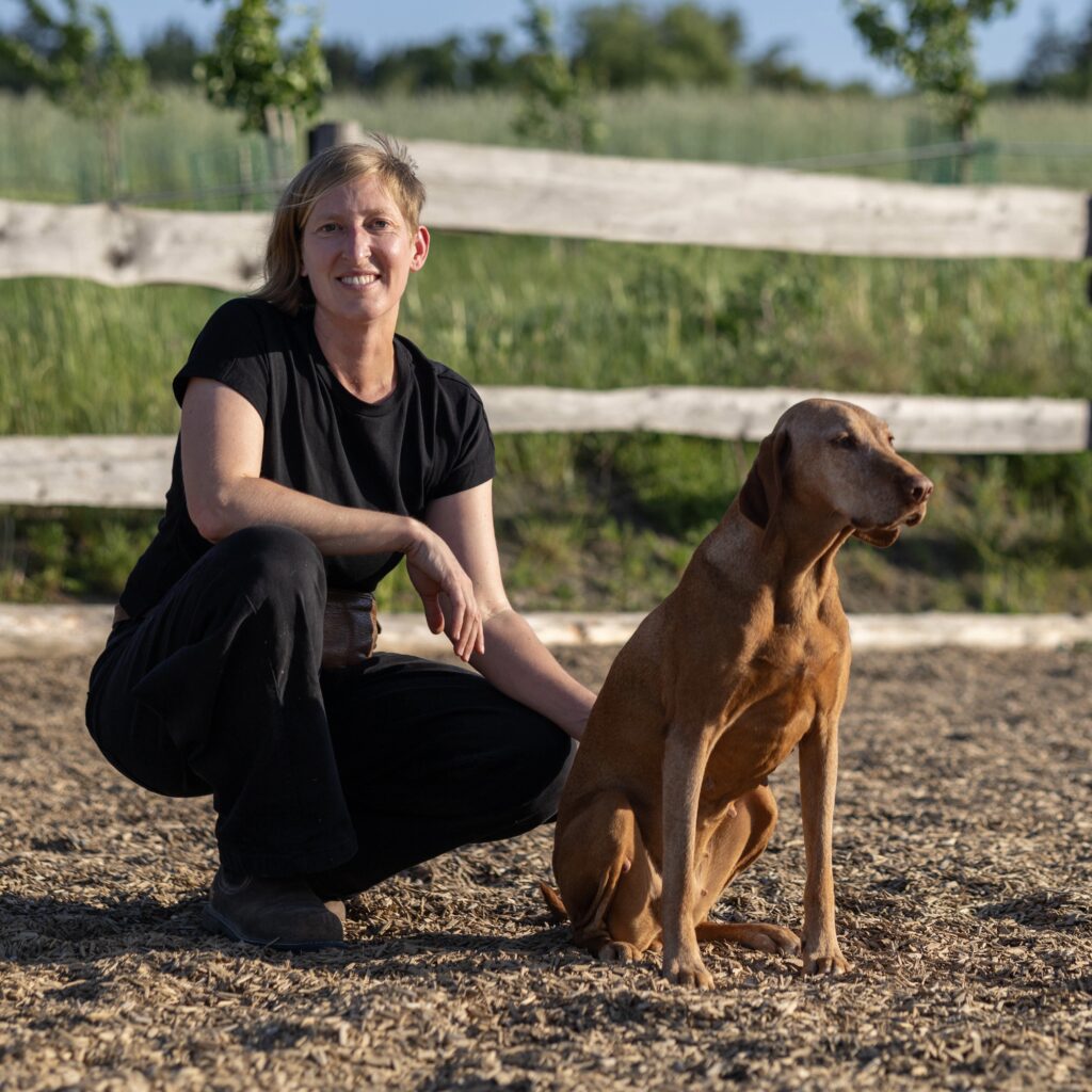 Hundeosteopathin Johanna Stöcker kniet neben einem braunen Hund.